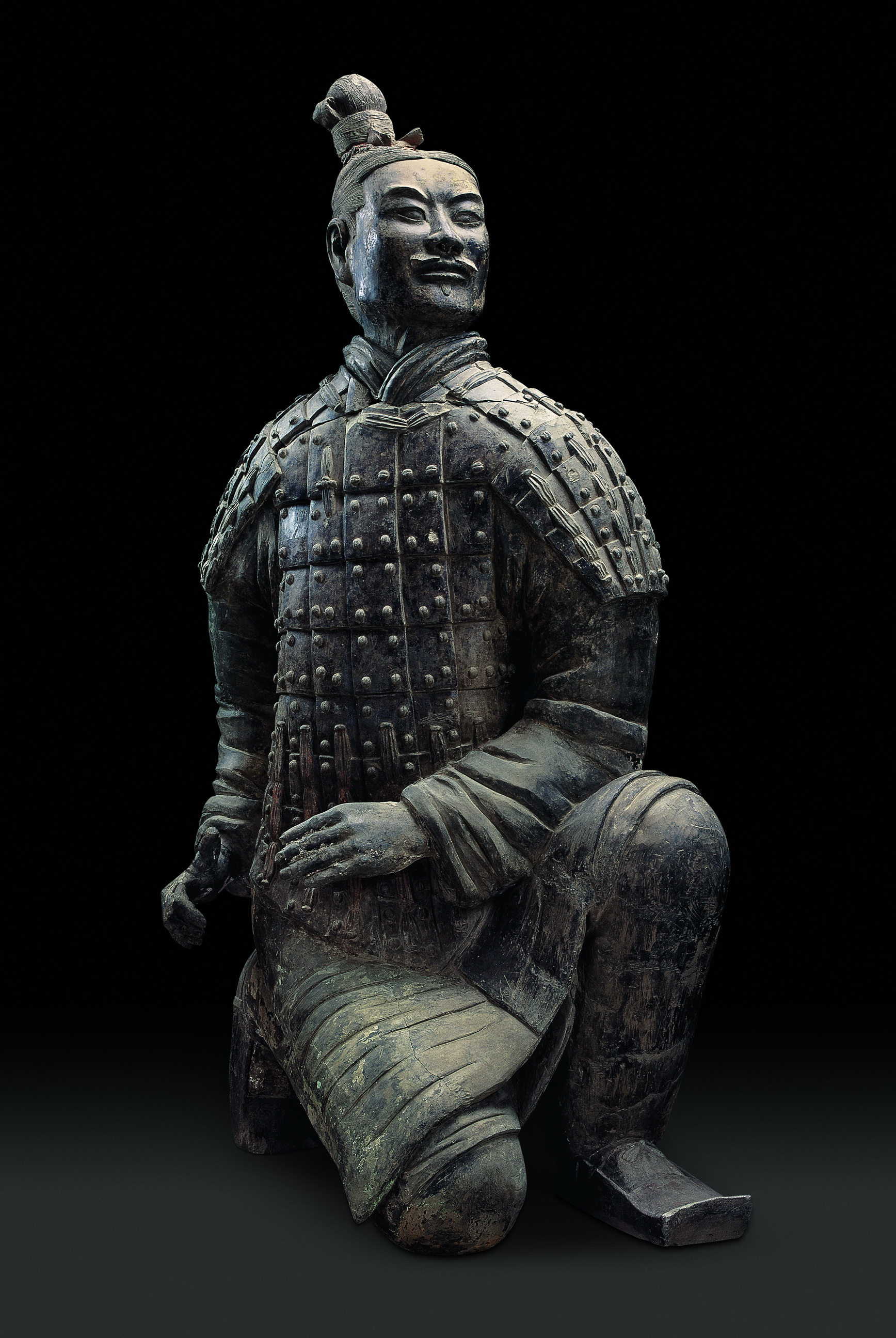 身穿战袍,外披铠甲,头顶右侧绾一发髻,左腿曲蹲,右膝着地,双手置于