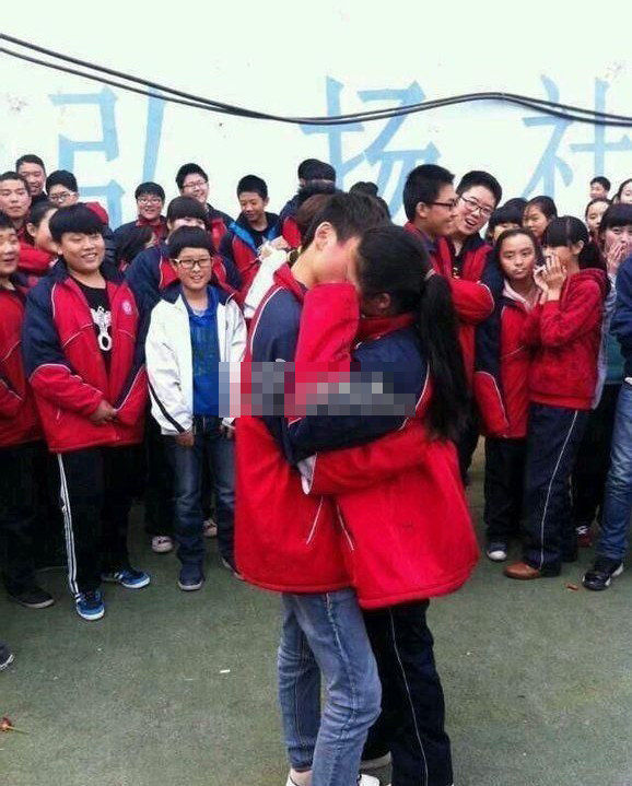 照片中一对穿着校服的初中生在学校操场当众求爱接吻,一旁围满了鼓掌